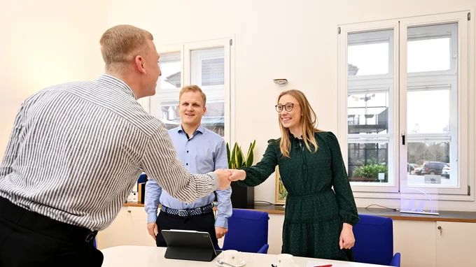 Zwei WOABU-Mitarbeitende (ein Mann und eine Frau) begrüßen einen Bewerber mit einem Handschlag. Die Personen lächeln sich an.