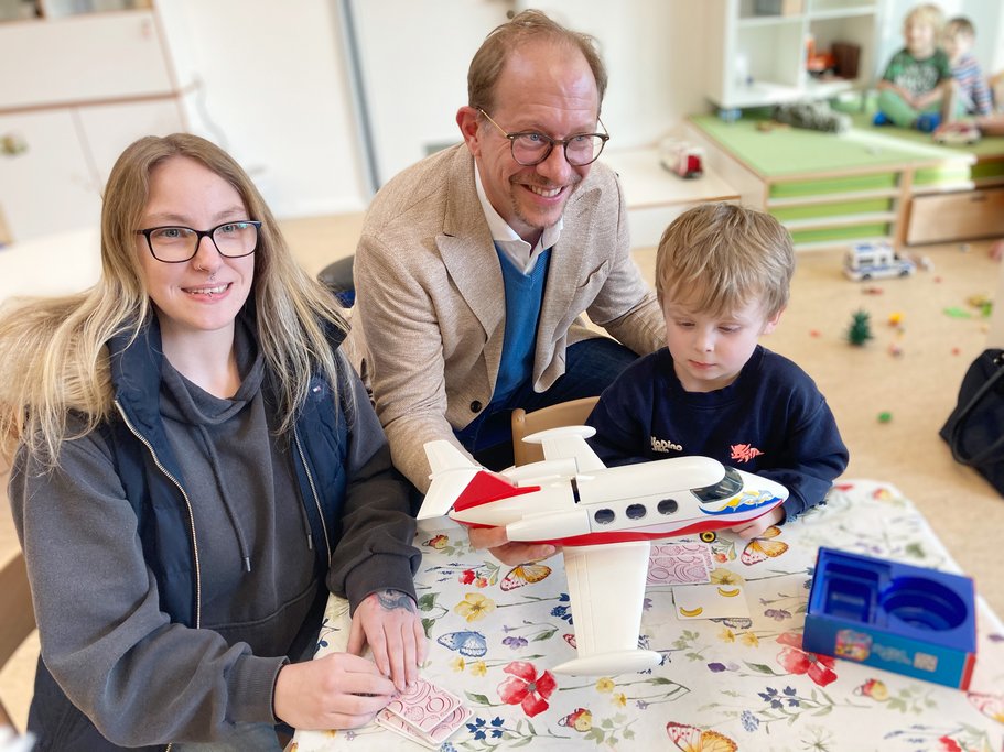 Mutter und Kind sitzen zusammen mit dem Oberbürgermeister Tobias Bergmann an einem Kindertisch.