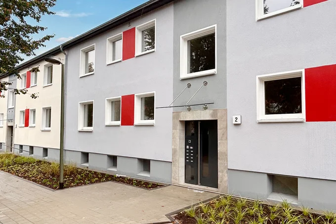 Eingang eines WOBAU-Wohngebäudes. Ein Weg führt zur Eingangstür, drumherum sind Beete angelegt.
